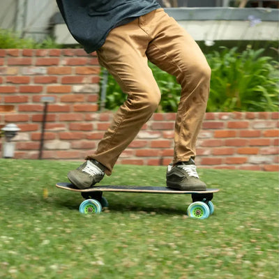 Person skateboarding on grass with a brick wall and plants in the background